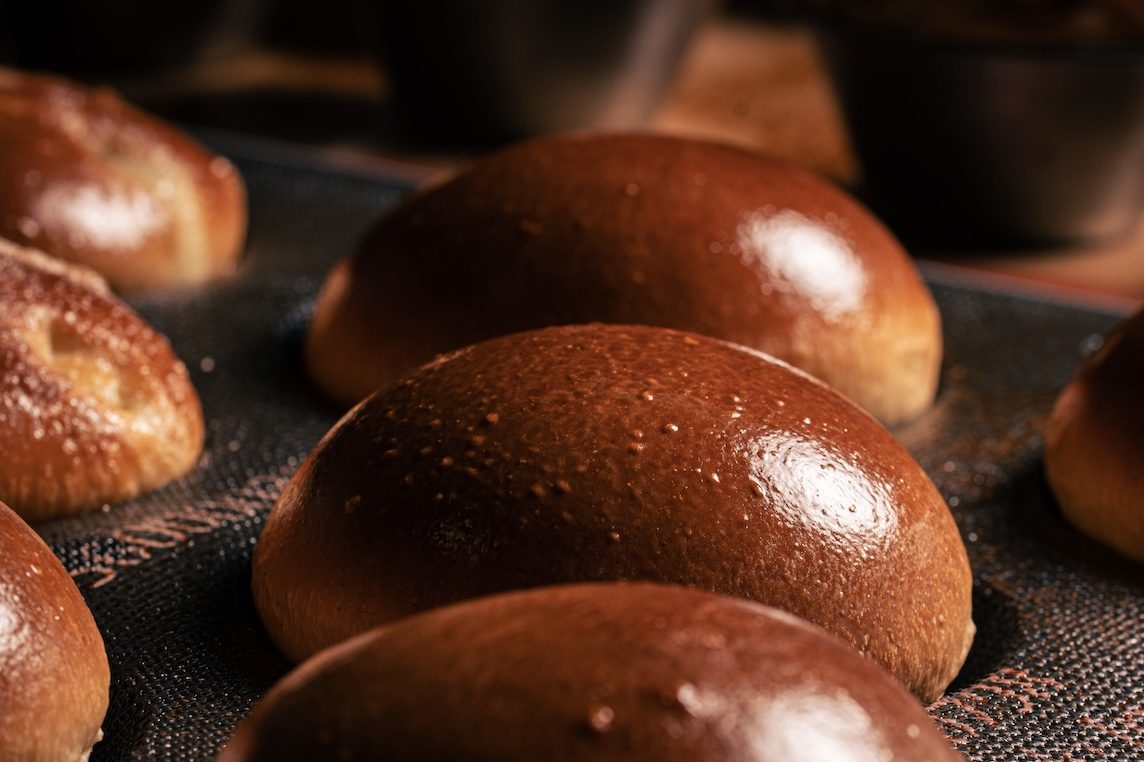 Freshly baked, glossy buns on a baking tray.