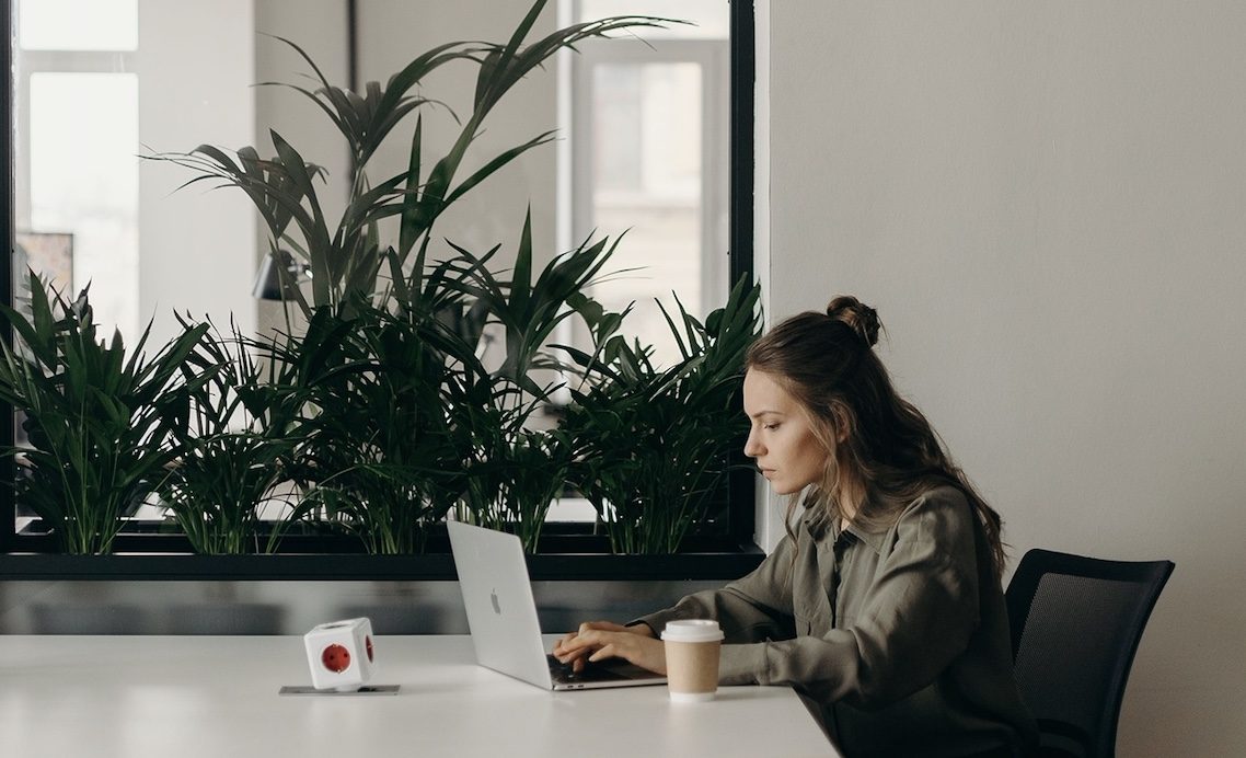 Woman working at a laptop in a bright room with green plants.